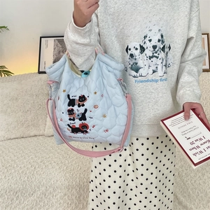 Close-up of a light blue quilted cat handbag with pink straps on a cream sofa