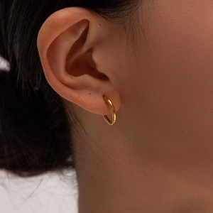 Gros plan de boucles d'oreilles créoles cœur plaqué or 18K sur l'oreille d'un modèle