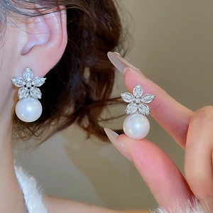 Close-up of elegant zircon flower earrings with pearl drops shown on model and held by hand