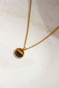 Close-up of a round tiger eye stone pendant on a gold chain over a textured stone base
