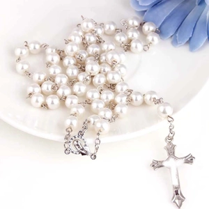 Détail du chapelet en perles blanches avec crucifix en argent sur une assiette blanche