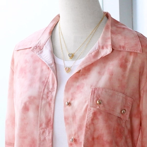 Close-up of double-layered heart pendant necklaces with pink crystal on tie-dye shirt