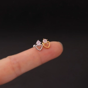 Detail of hollow heart-shaped earrings with pink zircon studs held on fingertips