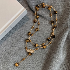 Detail of beaded tiger eye necklace with a crystal leaf pendant on gray knit fabric