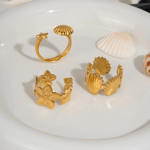 Bagues ouvertes dorées avec étoile de mer et coquillage sur un plat en céramique