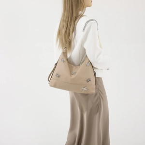 Beige shoulder bag with silver bows, chic hobo style shown on model with clean background
