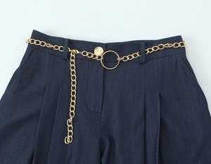 Détail d'une ceinture chaîne dorée avec boucle ronde sur un pantalon bleu marine