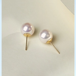 Classic white pearl stud earrings with gold metal base on minimalist cream background