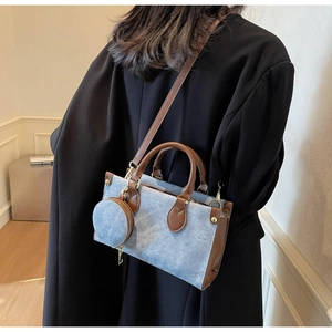 Détail du sac cabas en denim bleu avec anses en cuir marron et breloque porte-monnaie