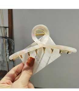 Detail view of twist-shaped acetate hair claw clip with golden metal spring and pearl finish
