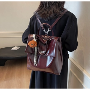 Detail of burgundy wax leather backpack with glossy texture and teddy bear pendant