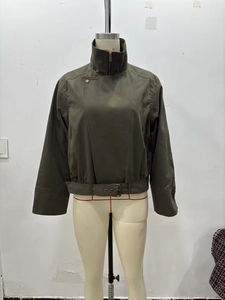 Detailed close-up of dark olive green cropped trench jacket with belt and stand collar