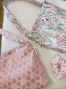 Pink floral heart pattern fabric handbag with matching scrunchie on white surface