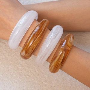 Detail of wide acrylic bangles in cream white and amber marble on stone background