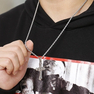 Detail of a silver stainless steel cross pendant and rope chain worn by a model in a hoodie