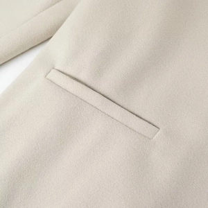 Dettaglio di una tasca a filetto su un cappotto lungo in lana beige strutturata