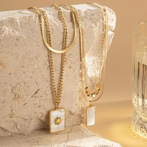 Layered gold titanium steel necklace with starburst shell pendants on natural stone