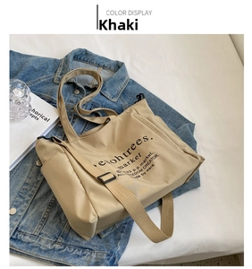 Detail view of khaki nylon tote bag with side pocket and black lettering on white surface
