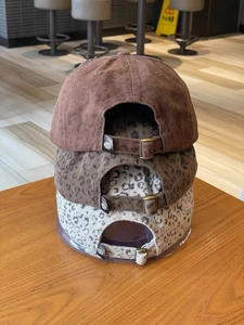 Detail view of adjustable metal buckle and stacked leopard print baseball caps