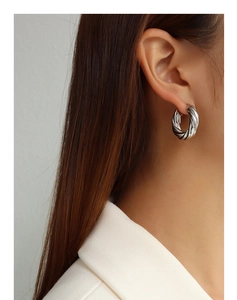 Close-up of thick silver twisted hoop earrings with a metallic finish on a model
