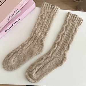 Detailed knit texture of khaki wool socks featuring classic cable pattern and leather tag