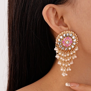 Detailed close-up of a gold floral earring with pink enamel and white pearl tassels