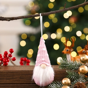 Close-up of pink knitted Christmas gnome hanging on tree with warm festive bokeh lights