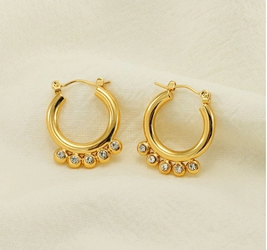 Detail of 18K gold hoop earrings featuring five sparkling white zircon stones on fabric