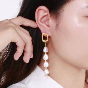 Gros plan de boucles d'oreilles pendantes dorées avec perles baroques blanches