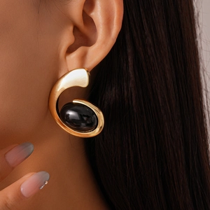 Close-up of golden irregular metal earring with a black oval resin inlay on a model