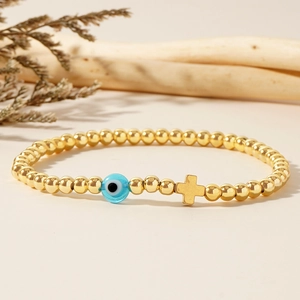 Bracelet à billes dorées avec perle œil bleu et pendentif croix sur fond naturel