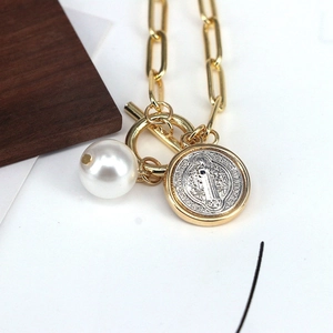 Detailed shot of a gold chain necklace with white pearl and religious coin pendant