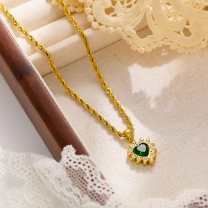 Detailed close-up of a golden heart pendant with green gemstone and white zircons