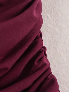 Detailaufnahme der gerafften Textur und des weinroten Satinstoffs von diesem Kleid