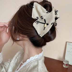 Macro detail of large beige fabric bow hair claw with elegant black ribbon and gold pendant