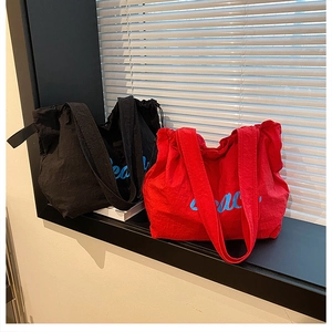 Close-up of black and red canvas tote bags with blue cursive printing on white background