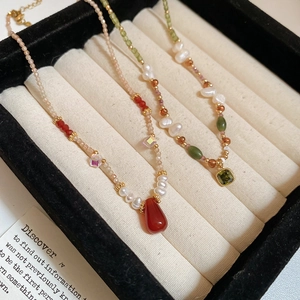 Detail of 18k gold plated freshwater pearl necklace with red and green gemstones