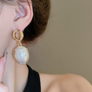 Close-up of elegant gold geometric earrings with large white oval imitation pearls on a model
