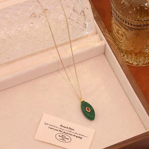 Détail d'un collier vintage doré avec un pendentif feuille verte et pierre rouge centrale