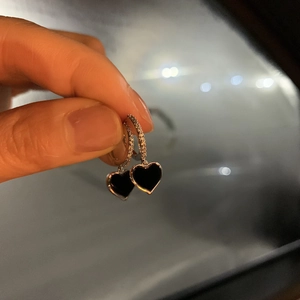 Detail of heart-shaped black drop earrings with sparkling pavé stone hoops held in hand
