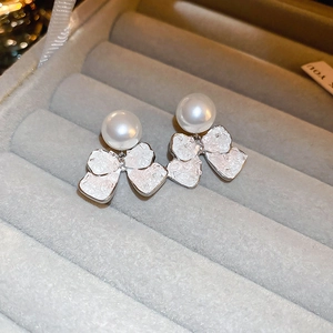 Macro shot of faux pearl and wrinkled texture silver bow stud earrings on jewelry tray