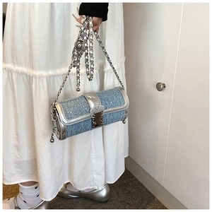 Close-up of denim blue cylinder bag with silver chain strap worn by a model in white dress