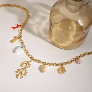 Detail of gold necklace featuring colorful coral, seahorse and seashell charms on beige background