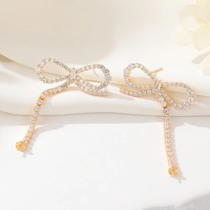 Detailed close-up of bow knot tassel earrings with white zircons on a golden base