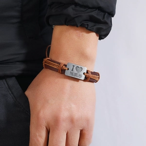 Detail of adjustable woven brown leather bracelet with an engraved heart metal plate