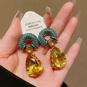 Detailed macro view of gold plated drop earrings with green pavé and yellow crystals