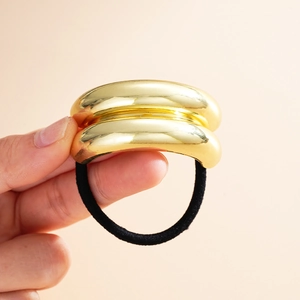 Elastic ponytail holder with premium gold metal finish ornament held in hand