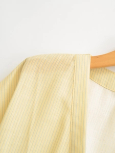 Detailed close-up of yellow striped kimono top shoulder with fine stitching on wooden hanger