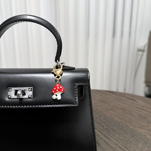 Detail of a red enamel mushroom keychain with pearl accent on a black leather handbag
