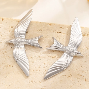 Macro shot of silver bird earrings featuring detailed feather textures on stone surface